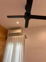 Ventilador de techo negro sobre el aire acondicionado de pared y la ventana con cortinas blancas